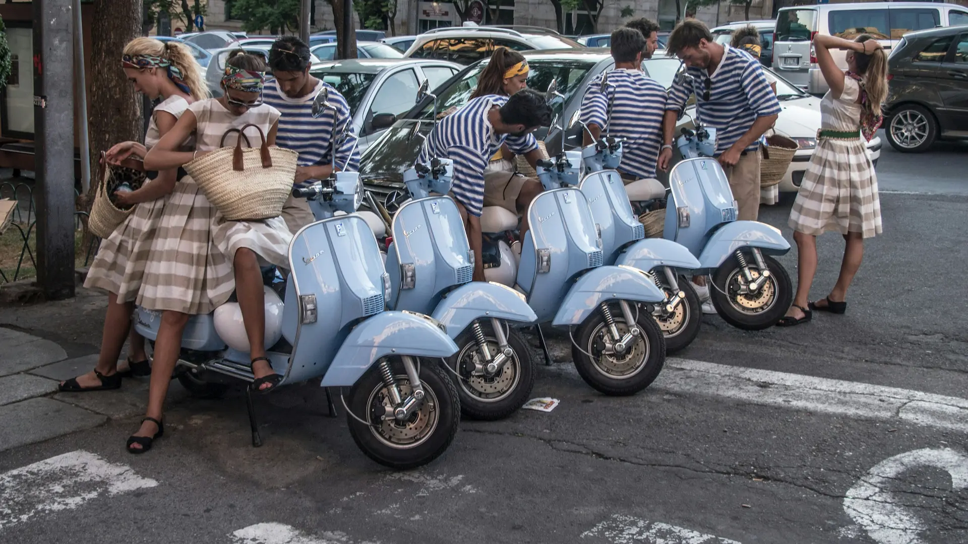 Photo of five couples in matching clothes next to their parked blue mopeds.