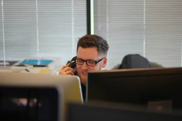 Man in glasses on the phone behind screens in an office environment.