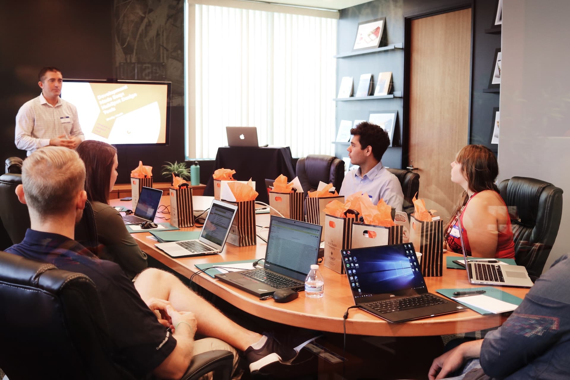 Six people in a board room listening to one of them presenting.