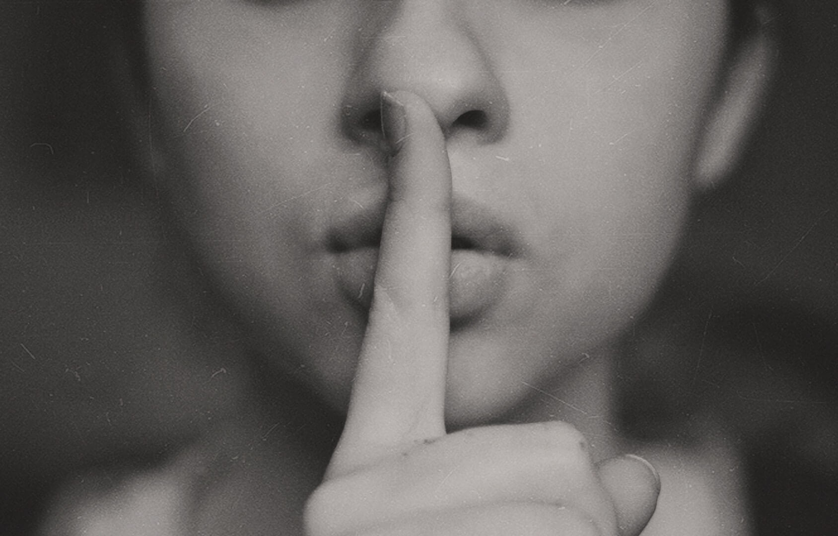 Photo of a woman putting her pointing finger in front of her mouth making a "shh" sound to keep quiet.