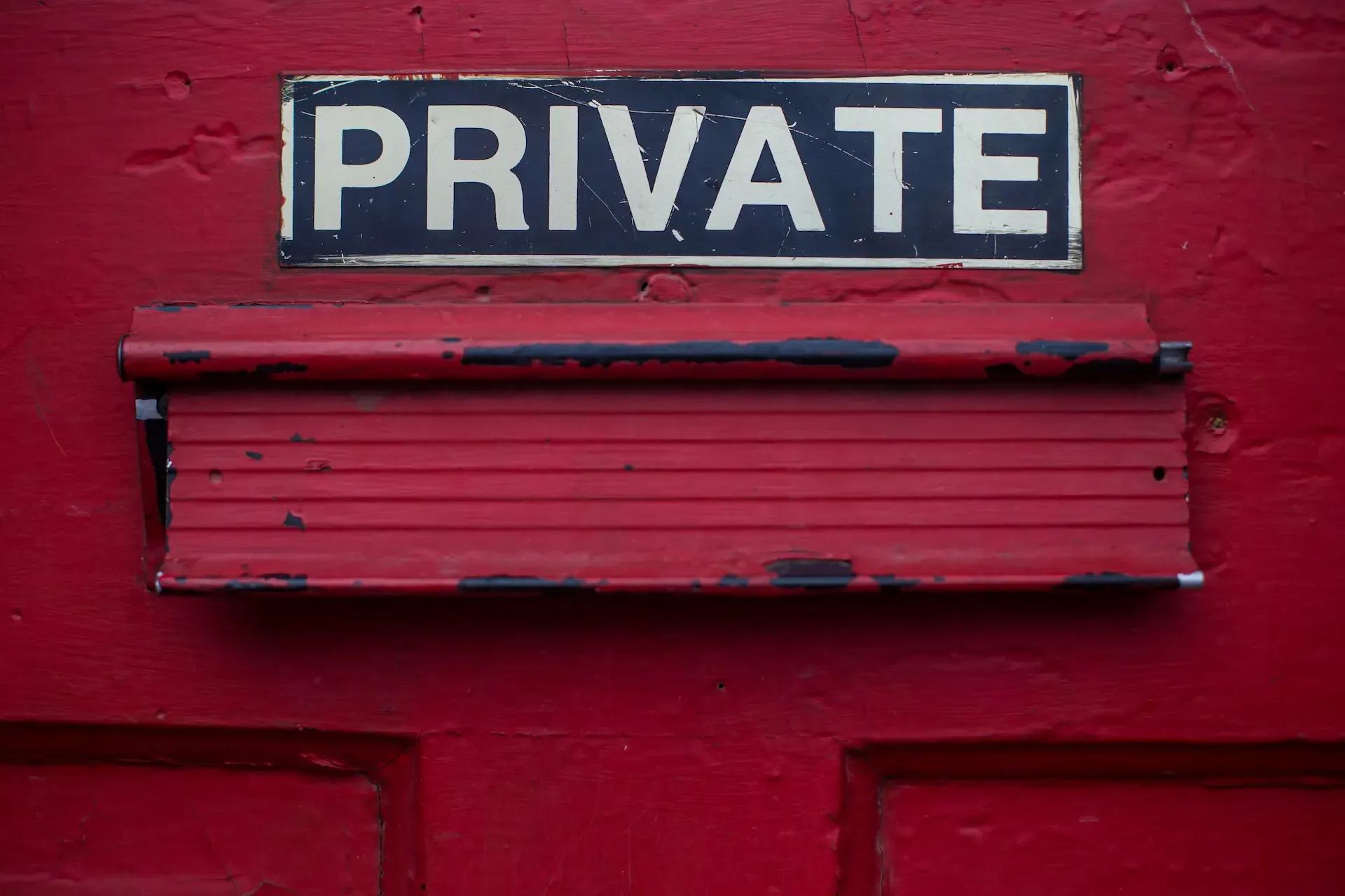 Closeup shot of a letter box on a red door with a sign above that says "private." 