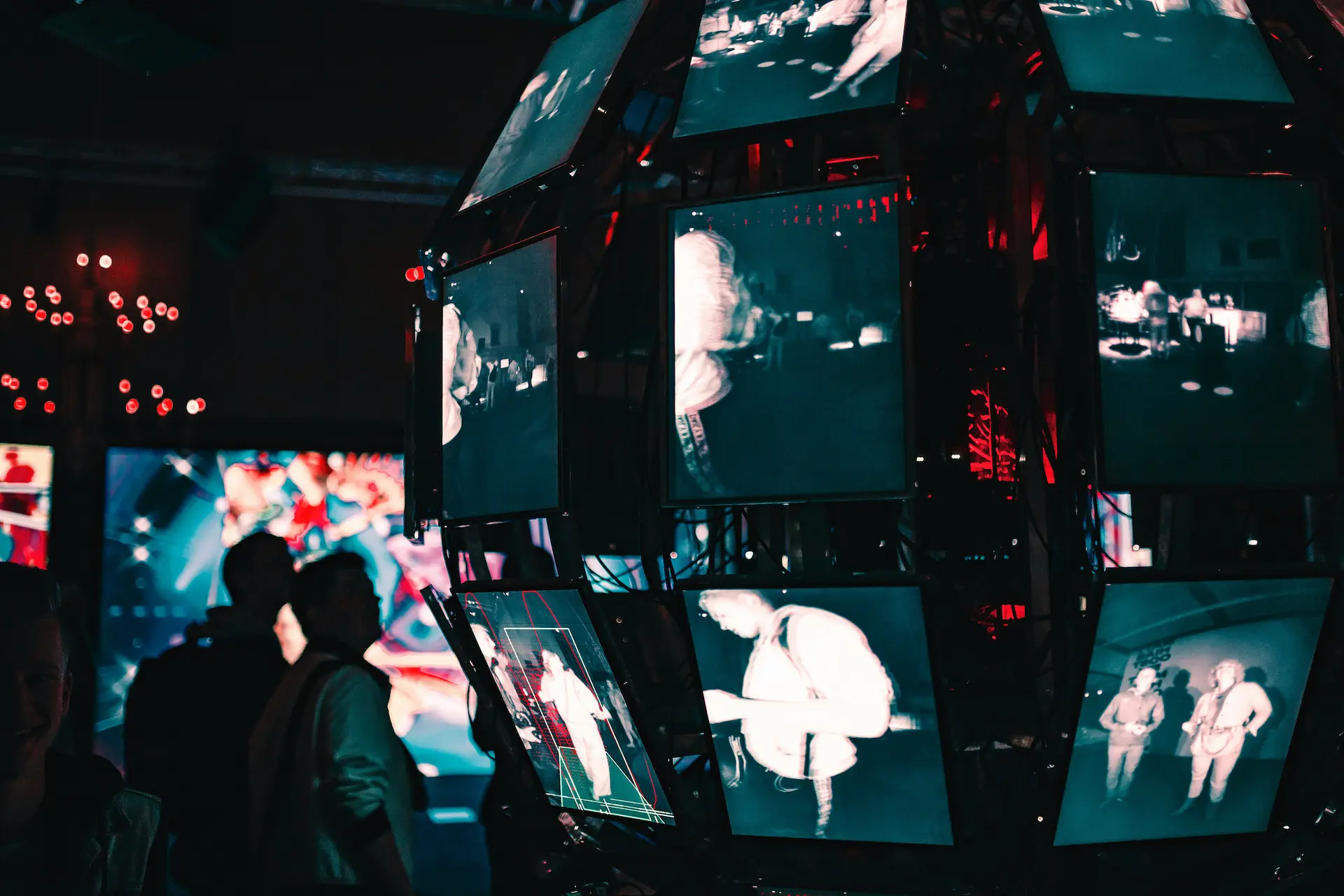 A night photo of a sphere made up of rectangular monitors with screens and silhouettes of people in the background.