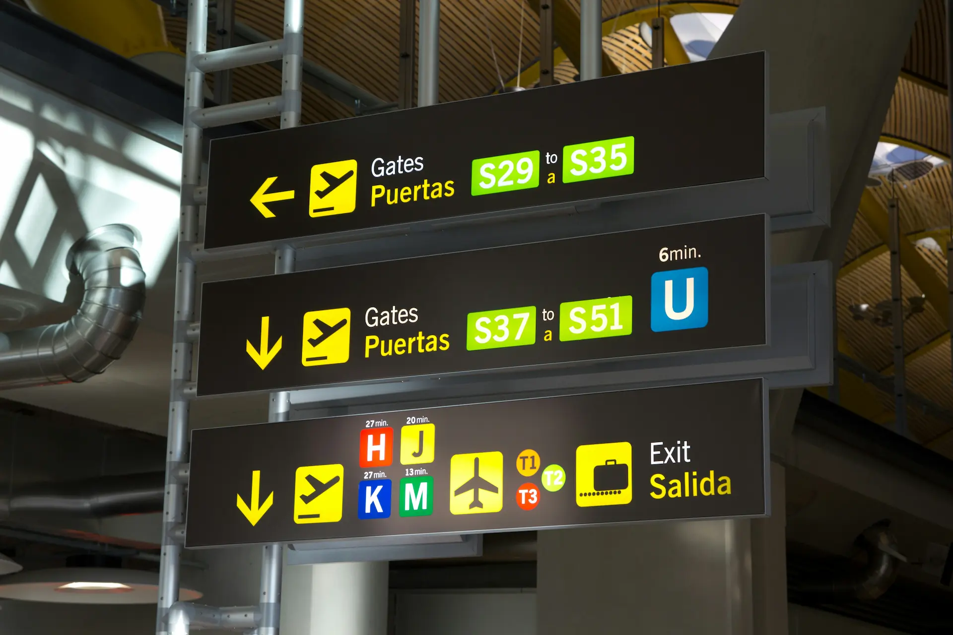 Signs in an airport with pictograms and text in English and Spanish.