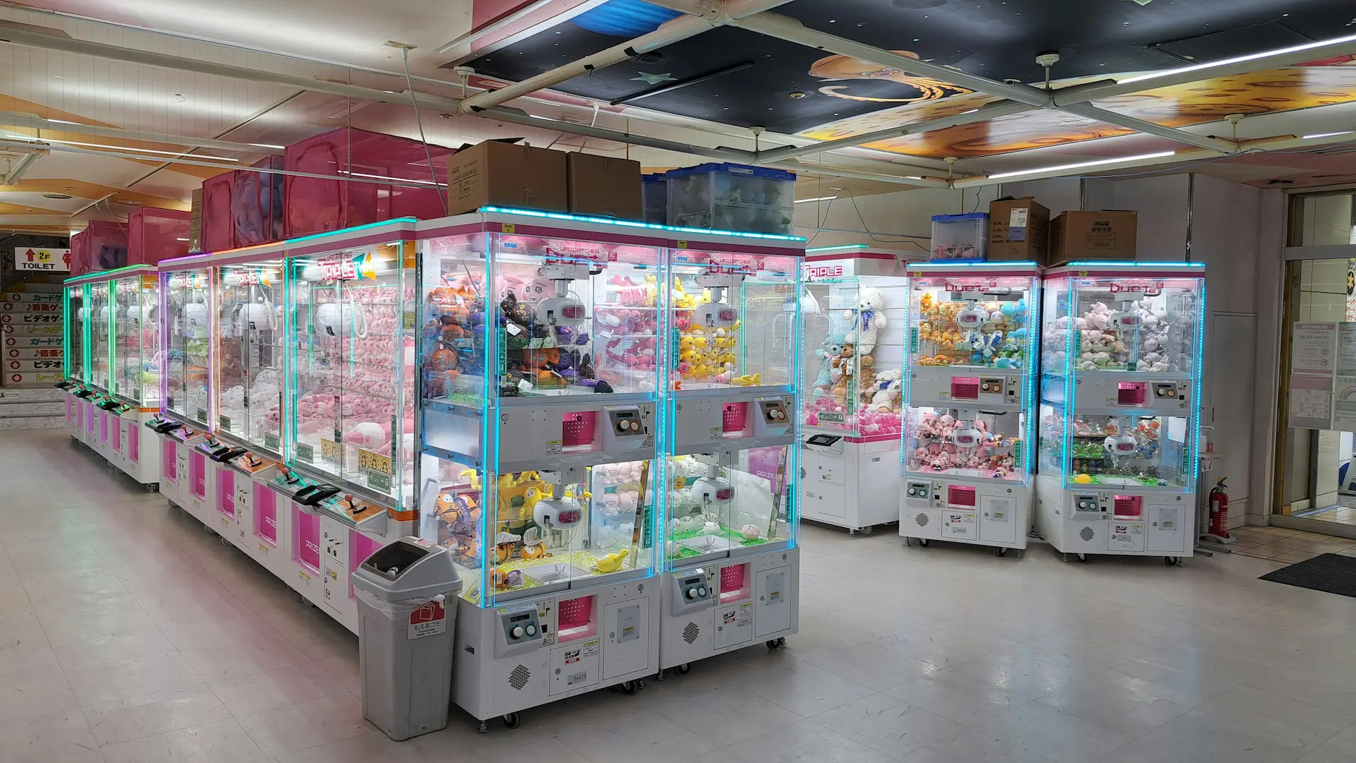 Cute pink and baby blue claw machines in an empty arcade filled with plushies.