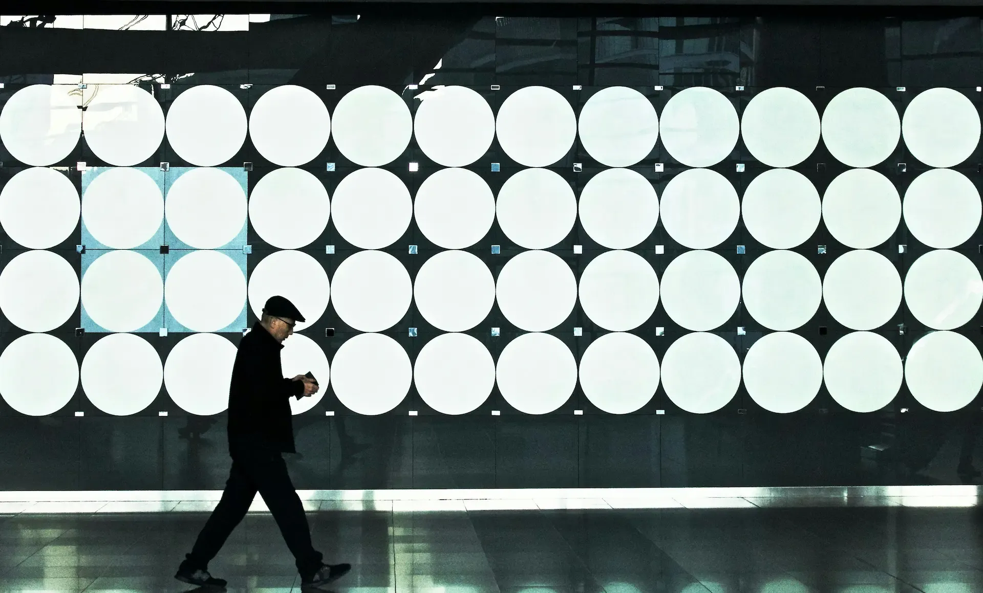 Man walking in front of a modern facade made of lots of large bright circles in a grid.