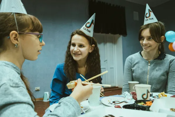 Three young women sitting at a TikTok themed party table eating sushi.