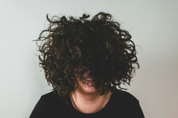 A woman with very curly hair that's covering her face. Her smile shines through.