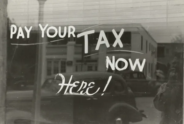 Photo of shop window from early 20th century with text "pay your tax now here!"