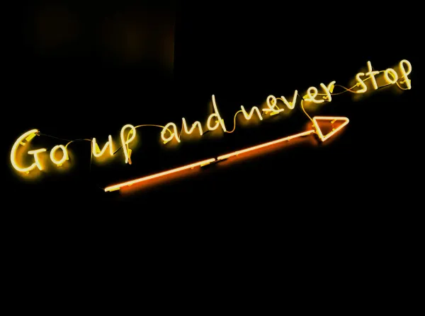 Neon sign that says "Go up and never stop" with a neon arrow pointing right under it.