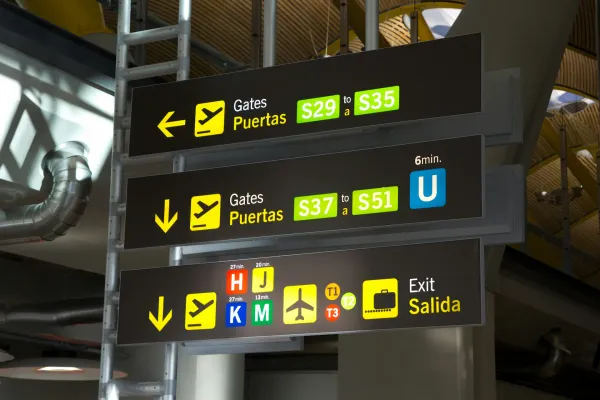 Signs in an airport with pictograms and text in English and Spanish.